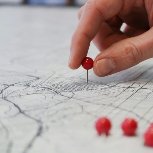 Hand tacking a red pin to a map of landscape