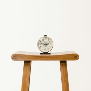 Alarm clock on wooden stool representing delayed action