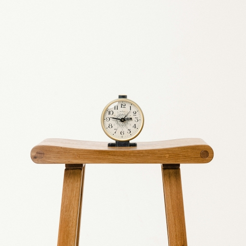 Alarm clock on wooden stool representing delayed action